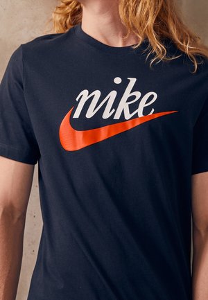 Persoon draagt een zwart T-shirt met het woord "mike" in het wit en een oranje swoosh-logo op de borst.