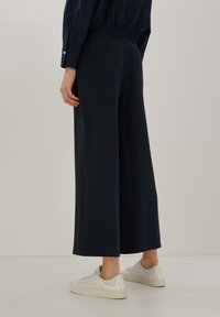 Marinblå vida byxor i mjukt tyg med resårmidja, i kombination med vita sneakers. Sömlös design för ökad komfort.