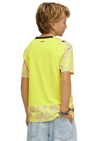 Chemise de sport jaune à manches courtes avec tissu texturé, manches à motif et accents noirs. Présente un motif graphique à l'ourlet.