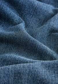 Denim stof in een donkerblauwe kleur, met een gestructureerde weving en subtiel diagonaal patroon, gedrapeerd met zachte plooien.