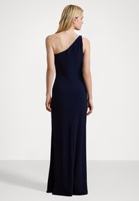Marinblå klänning med en axel i stretchigt material, med figurnära överdel och flödande kjol med en slit bak, stilren och minimalistisk design.
