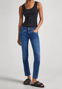 Blå denimjeans med en figursydd design, med en knappstängning och ett framfick. Parat med en svart linne och svarta sandaler.