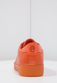 Oranžové kožené tenisky s hladkým povrchem, kulatou špičkou a plochou podrážkou. Nabízí logo na patě a pevný design šněrování.