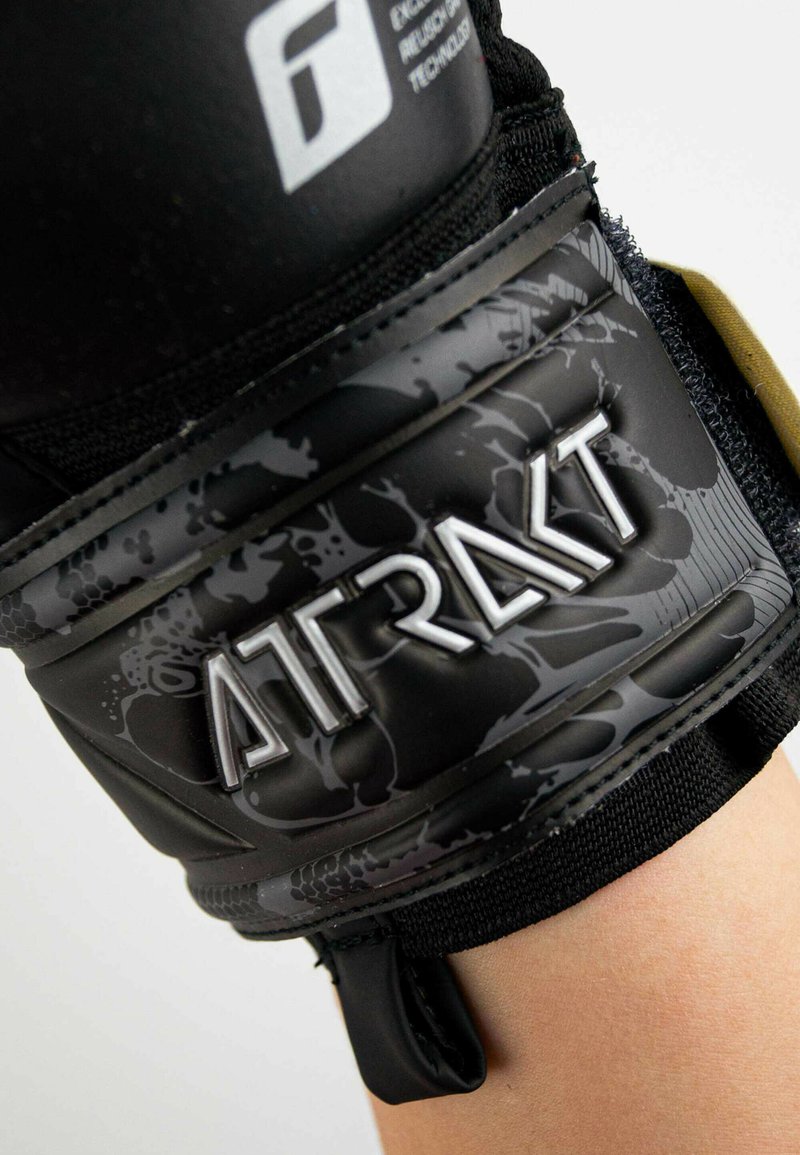 Supporto per polso nero con design testurizzato, cinturino regolabile e logo riflettente "ATRAKT" su una base opaca con motivi sottili.