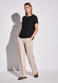 Sort top med struktureret strik ved skulderpartiet, beige brede bukser og sorte mesh flats. Simpel design med afslappet pasform og lommer.