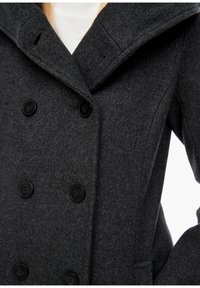 Manteau en laine gris foncé à double boutonnage avec de grands revers, six boutons noirs, et des poches latérales, porté sur un haut blanc côtelé.