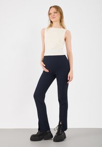 Cream sleeveless top with a square neckline paired with fitted navy pants featuring side slits. Black chunky-soled lace-up boots complete the look.