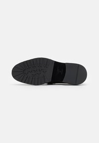 Suola di scarpa nera con gomma testurizzata, caratterizzata da una forma arrotondata, una presa a motivo e bordi lisci. Branding visibile sulla suola.