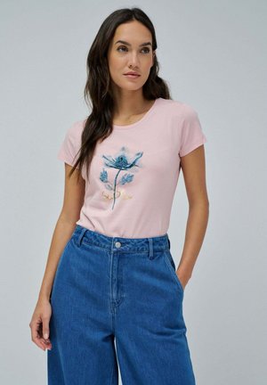 Rosa Baumwoll-T-Shirt mit blauer Blumenstickerei und goldener Schrift. Rundhalsausschnitt und kurze Ärmel. Kombiniert mit hochgeschlossenen blauen Denim-Hosen.