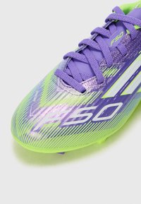 Chaussure de football violette vibrante avec un design texturé, des accents verts, un logo 'F50' blanc et des lacets violets. Convient pour le gazon.