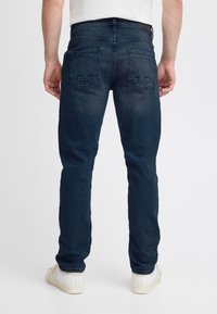 Mørkeblå denimjeans med smal passform, med to baklommer og lett slitasje. Kombinert med hvite joggesko.