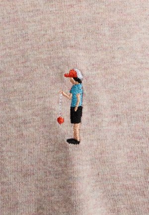 Geborduurd figuur van een persoon die een rode pet, een blauw shirt en een zwarte korte broek draagt, en een rode bal aan een touw vasthoudt tegen een lichte stof.