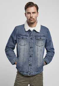 Giubbotto in denim con colletto in pelliccia sintetica bianca, due tasche sul petto, chiusura a bottoni e un lavaggio azzurro sbiadito, caratterizzato da dettagli di cucitura verticale.