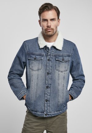 Denim jacket with a white faux fur collar, two chest pockets, button closure, and a faded blue wash, designed with vertical stitching details.