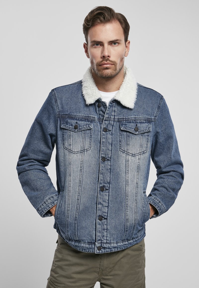 Giubbotto in denim con colletto in pelliccia sintetica bianca, due tasche sul petto, chiusura a bottoni e un lavaggio azzurro sbiadito, caratterizzato da dettagli di cucitura verticale.