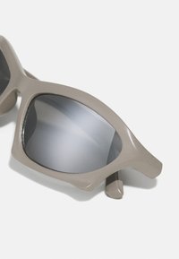 Grijze zonnebril met een dik, hoekig frame en spiegelende lenzen. Het materiaal heeft een gladde, glanzende afwerking en minimale details.