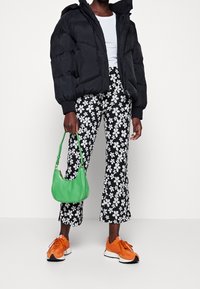 Svart pufferjacka, vit topp, blommiga svartvita byxor, grön handväska och orange sneakers. Strukturerad tyg, kort design, livfulla färger.