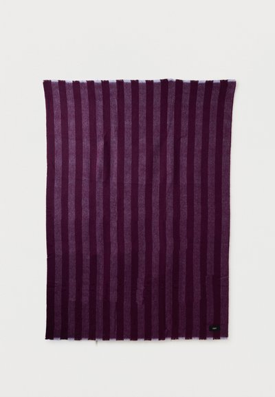 Ορθογώνιο ύφασμα με κάθετες ρίγες σε εναλλασσόμενες αποχρώσεις σκούρου μωβ και λεβάντας, απλωμένο επίπεδα με μια μικρή μαύρη ετικέτα στην κάτω δεξιά γωνία.
