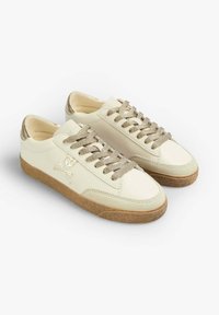 Weiße Leder-Sneaker mit goldenen Akzenten, strukturierten Schnürsenkeln und einer braunen Gummisohle, die ein Totenkopf- und Kreuzbeinmuster an der Seite aufweisen.