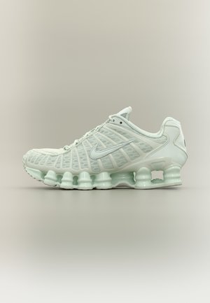 Chaussure de course Nike blanche avec tige en maille translucide, coussins d'amortissement visibles sur la semelle, et logo Nike swoosh argenté sur le côté.