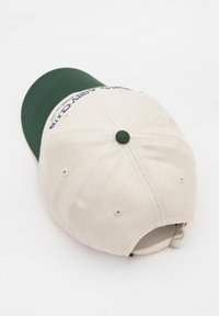 Cappellino da baseball colore crema con visiera verde, dotato di testo ricamato, fori di ventilazione e cinturino regolabile sul retro.