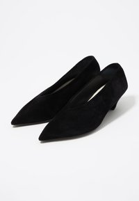 Décolleté in suede nero con punta affusolata e tacco a blocco basso. Presentano una texture liscia e un design con ritagli sui lati per un tocco di dettaglio.