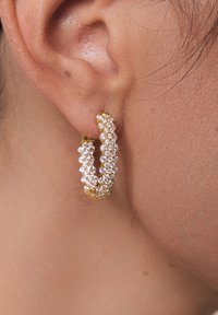 Złote kolczyki w kształcie koła zdobione wieloma małymi przezroczystymi kryształkami, charakteryzujące się zaokrąglonym kształtem i teksturowaną powierzchnią.