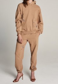 Sweat à capuche marron et joggers assortis en tissu doux, avec des accents de peinture éclaboussée et des détails usés, dotés de poignets et d'une taille élastiques.