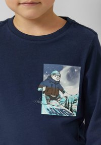 Granatowa koszula z długim rękawem z grafiką misia jeżdżącego na snowboardzie. Miękka tkanina, okrągły dekolt i luźny krój z nadrukiem.