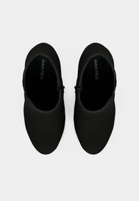 Zapatos negros tipo slip-on con una textura lisa y mate, punta en forma de almendra y un adorno de hebilla lateral. Etiquetados con "ANNA FIELD" en el interior.