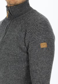 Maglione grigio a coste con colletto alto, dotato di mezza zip e un'etichetta del marchio beige sulla spalla sinistra. Tessuto a maglia testurizzato.