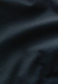 Tejido negro con una textura suave y ligeramente brillante, y un patrón de costura en diagonal. El material parece ser un textil de tejido resistente.
