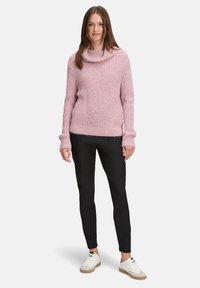 Chunky rosa gestrickter Pullover mit einem übergroßen Kragen, gerippten Ärmeln und lockerer Passform, kombiniert mit eleganten schwarzen Hosen und weißen Sneakers.