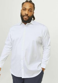 White long-sleeve button-up shirt made of smooth fabric, featuring a classic collar, side pockets, and a curved hemline.