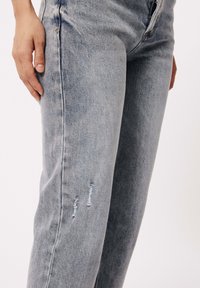 Lichtgrijze denim jeans met een rechte pijp, voorzien van versleten details op de dij en subtiele vervagingen door de stof.
