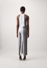 Halternekkjurk in grijs met witte strikdetails. Heeft een hoge split en een gladde, glanzende textuur. Draag het met zwarte schoenen en neongroene accenten.