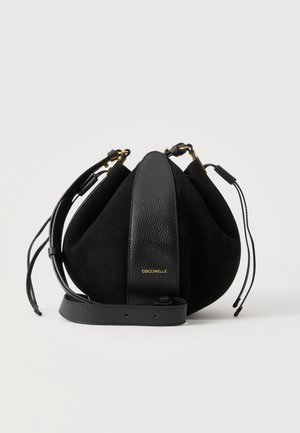 Sac seau en cuir et suède noir avec bandoulière réglable, fermeture par cordon et logo doré « Coccinelle » au centre devant.