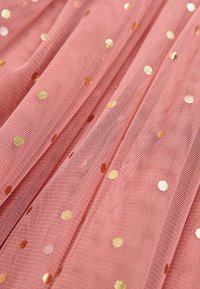 Tissu rose transparent avec des pois métalliques dorés, présenté en plis doux et en gros plan.
