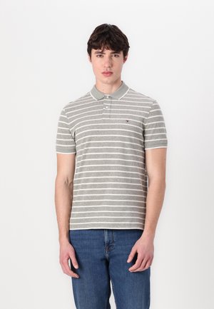 Polo a righe grigie e bianche con colletto, dotato di un piccolo logo sul petto, abbinato a jeans in denim blu.