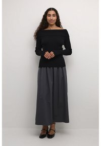 Juodas off-shoulder raštuotas megztinis su ilgomis rankovėmis, derinamas su grindims siekiančia tamsiai pilka sijoną ir juodais plokščiais batais; lygus paviršius.