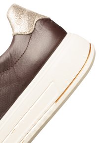 Brown leather sneaker heel with white thick sole and metallic gold accent on heel collar against white background.