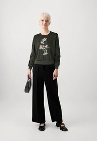 Tmavě zelená mikina s květinovým motivem, široké černé kalhoty, černé boty a šedá kabelka. Jednoduchý design, volný střih a nařasené manžety.