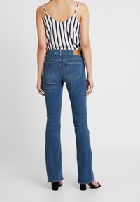 Jean denim bleu à jambes évasées avec un design à cinq poches et des coutures discrètes sur les poches arrière, associé à un débardeur rayé noir et blanc.