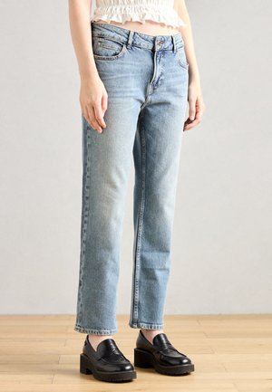 Jean en denim bleu clair avec une coupe droite, cinq poches et une finition délavée. Associé à des mocassins à plateforme noirs.