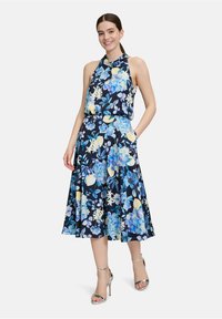 Blumenmusterkleid mit navyfarbenem Hintergrund, blauen und gelben Blumen, Halterneck, fließendem Rock und seitlichen Taschen.