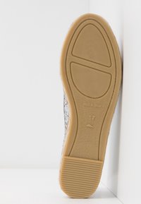 Semelle d'une chaussure, présentant une base en caoutchouc texturé de couleur marron clair avec des stries. L'étiquette indique "Fabriqué en Espagne" et la taille 37.