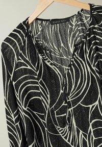 Blusa nera con un motivo fogliato bianco, tessuto leggero, chiusura con bottoni e scollatura a V con dettagli plissettati.