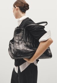 Borsa a tote in pelle nera con texture a coccodrillo, dotata di manici doppi, forma rettangolare e un design interno spazioso.