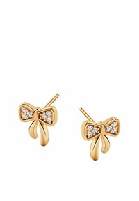 Złote kolczyki w kształcie kokardy z błyszczącymi, przezroczystymi kamieniami na środku. Gładka metalowa tekstura z dwoma końcami przypominającymi wstążki.