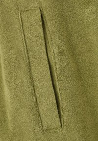 Close-up of olive green terry cloth fabric with a rectangular sewn-on tab detail.